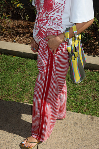 Person wearing a red checkered dress with colorful shoes on a grassy area.