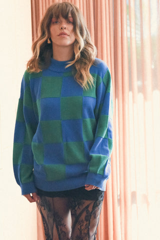Person wearing a blue and green checkered sweater in front of pink curtains.