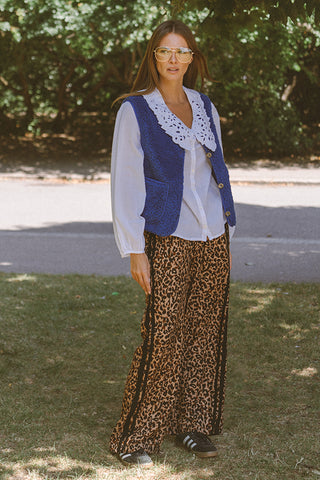 Woman wearing a blue vest over a white blouse and leopard print pants outdoors.