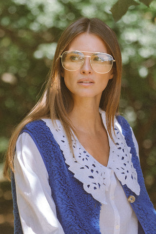 Woman wearing a blue knitted vest over a white blouse with a blurred natural background