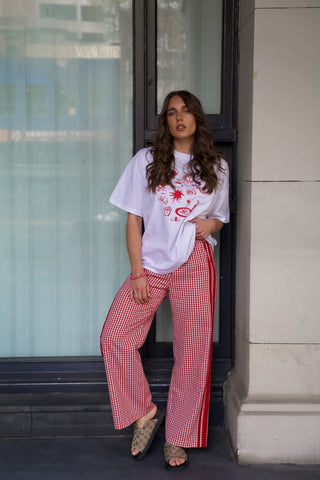 Woman wearing a white t-shirt with a graphic design and red checkered pants standing against a building.