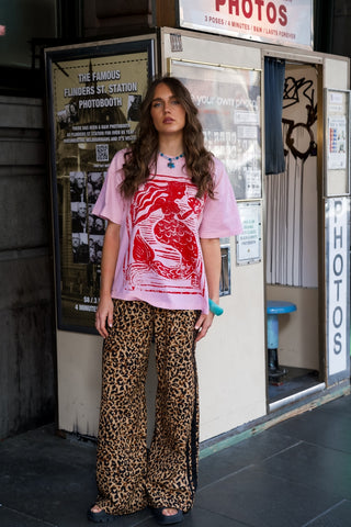 Person wearing a pink shirt with red graphic and leopard print pants standing in front of a photo booth.