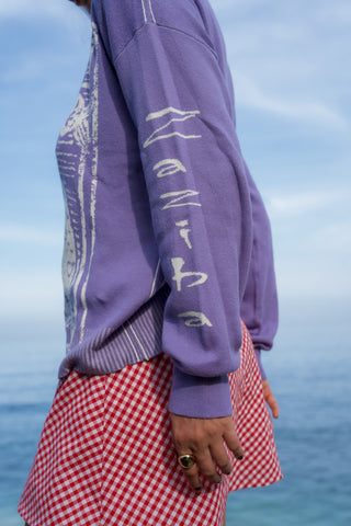 Person wearing a purple hoodie with text and a red checkered skirt against a blue sky.