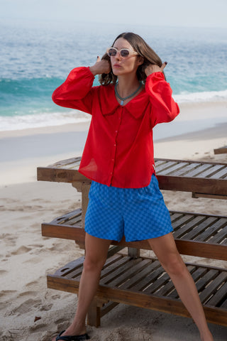Woman in red shirt and blue shorts standing on a beach with ocean view