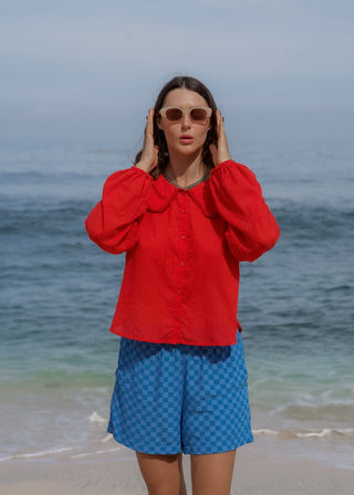 Woman in red shirt and blue shorts standing on a beach with ocean in the background