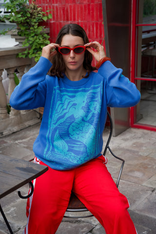 Person wearing a blue sweater with a tiger design and red pants, sitting outdoors.