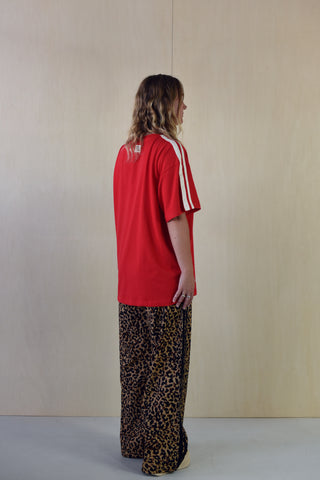 Person wearing a red shirt and leopard print pants against a plain background