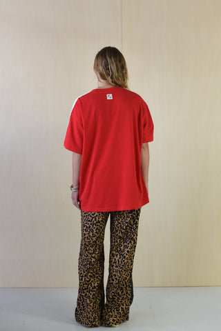 Person wearing a red oversized t-shirt and leopard print pants against a plain background