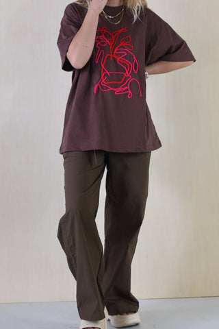 Person wearing a brown t-shirt with a red graphic design and brown pants on a plain background