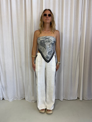 Woman standing against a white curtain wearing a silver dress and white pants.