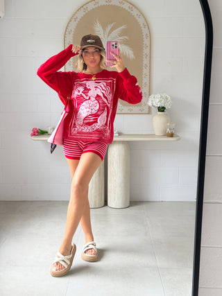 Person taking a mirror selfie wearing a red outfit with a graphic design, standing in a room with a decorative mirror and table.