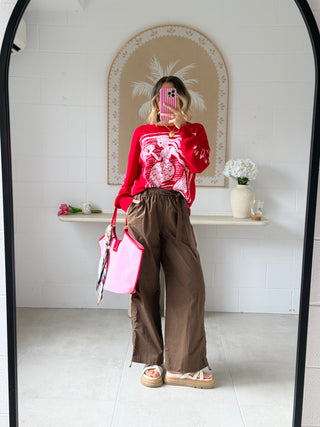 Person taking a mirror selfie wearing a red sweater and brown pants in a room with white walls and decorative elements.