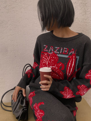 Person wearing a black sweatshirt with red designs and text, holding a coffee cup.