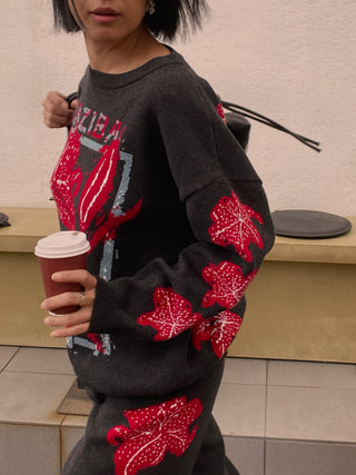 Person wearing a black sweater with red leaf patterns, holding a coffee cup.