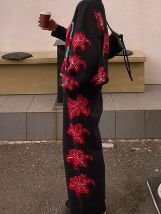 Person wearing a black outfit with red floral patterns, holding a coffee cup outdoors.