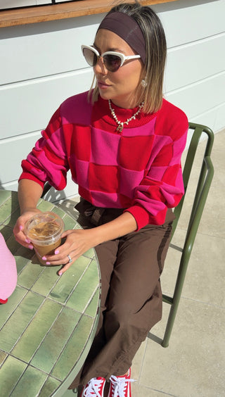 Person wearing a colorful sweater and sunglasses, sitting at an outdoor table.