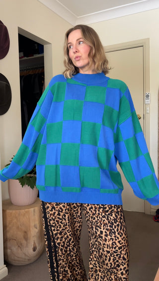 Person wearing a blue and green checkered sweater with leopard print pants indoors.
