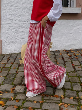 Person wearing red checkered pants and white shoes on a stone pavement.