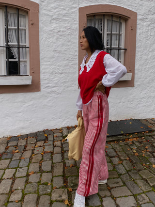 Person wearing a red and white outfit with a checkered skirt standing in front of a white wall with windows.