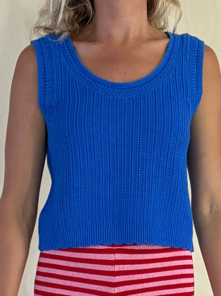 Person wearing a blue knitted tank top and red striped pants against a neutral background