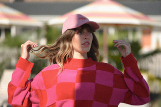 Woman wearing a pink checkered sweater and pink cap outdoors