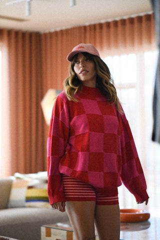 Person wearing a red and pink checkered outfit with a matching cap indoors.
