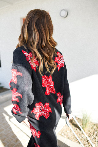 Person wearing a black sweater with red floral patterns, standing in an outdoor setting.